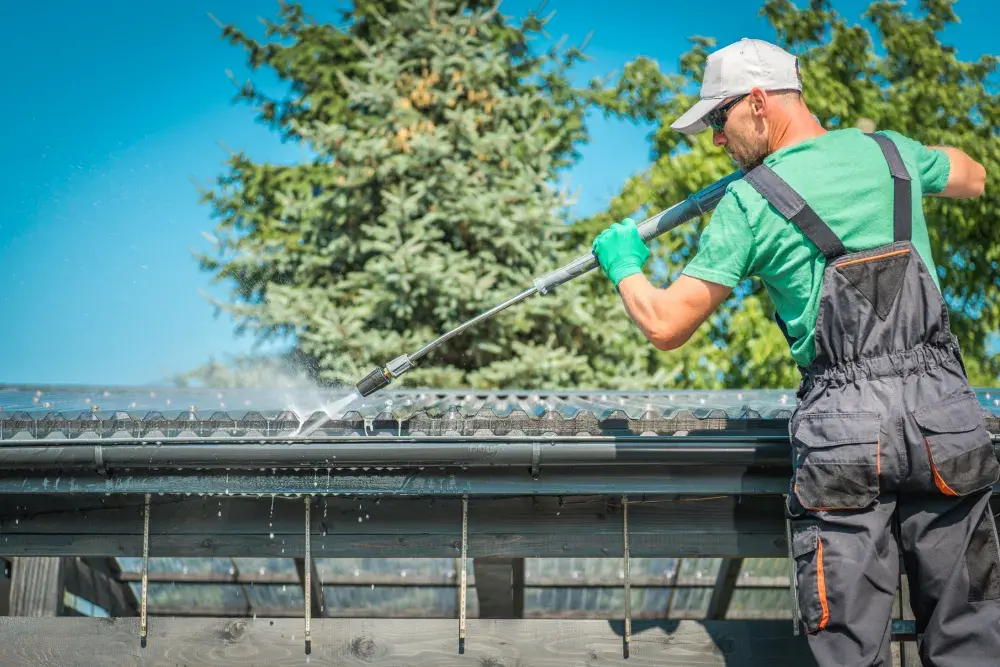 Worker cleaning roof gutters with pressure wshing